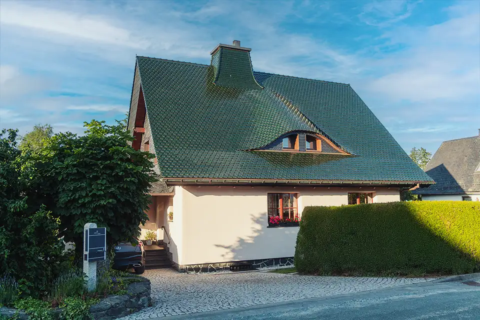 Curved dark slate roof with an attached rusty vertical pipe or antenna against a partly cloudy sky.