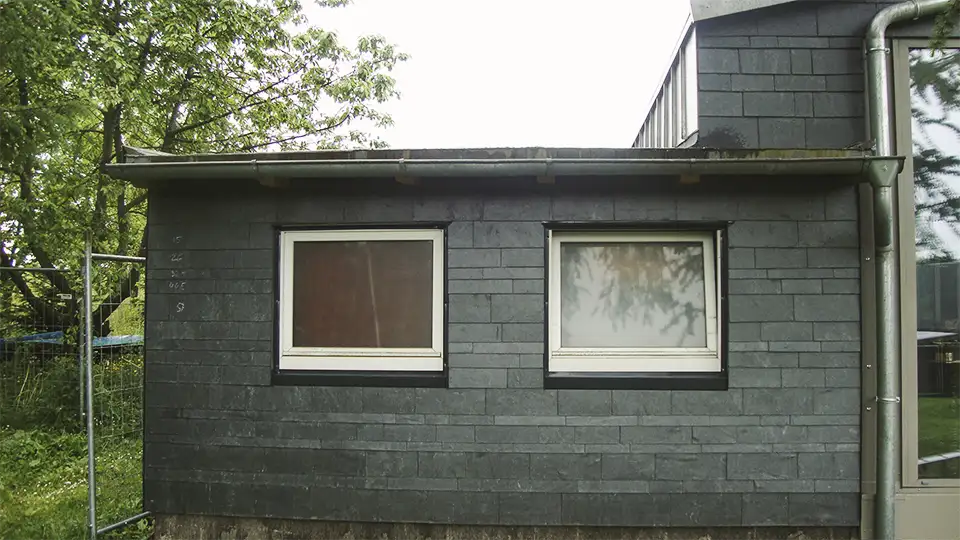 Wood-framed window set in dark slate-tiled roof with copper edging on a building under scaffolding.