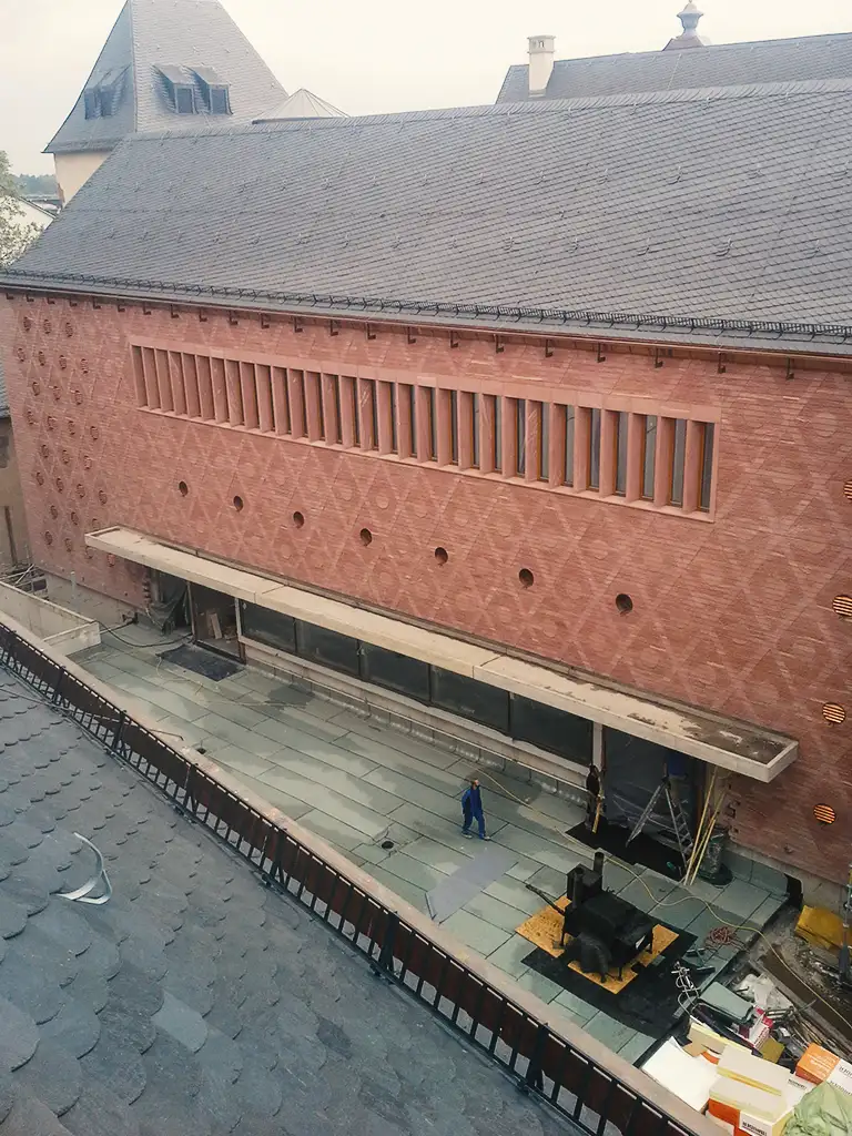 Copper roof structure with vertical supports viewed from above with scaffolding and trees in background.