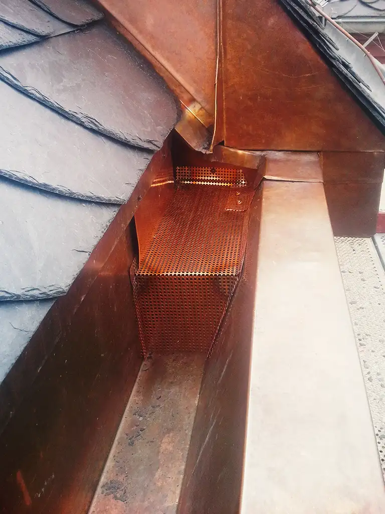 Copper roof structure with vertical supports viewed from above with scaffolding and trees in background.
