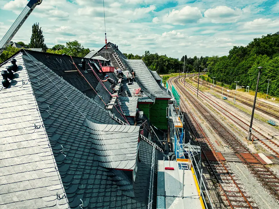 Curved dark slate roof with an attached rusty vertical pipe or antenna against a partly cloudy sky.