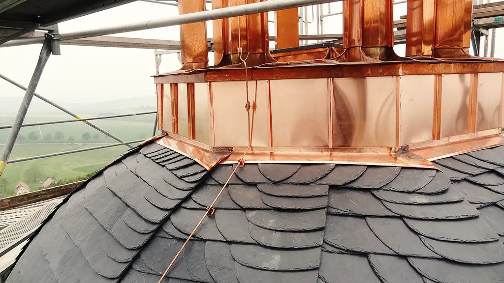 Copper roof structure with vertical supports viewed from above with scaffolding and trees in background.