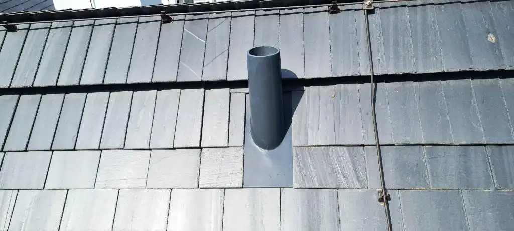 Curved dark slate roof with an attached rusty vertical pipe or antenna against a partly cloudy sky.